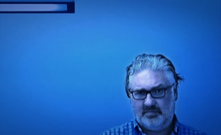 Im täglichen Geschäftsbetrieb präsent zu sein heißt für mich Verantwortung wahrnehmen - Inhaber und Geschäftsführer Marcel Sternke - Portraitfoto Geschäftsführer Marcel Sternke vor blauer Bürowand mit Deckenleuchte