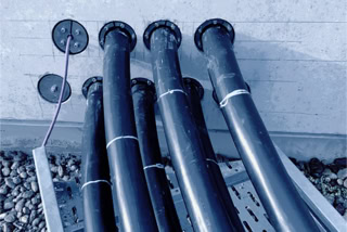Sieben Oberschenkel dicke, schwarz ummantelte Niederspannungskabel auf metallender Kabeltrassen-Konstruktion verschwinden in Betonwand - Projekt Produktionsanlage Solarlux - Sieben Oberschenkel dicke, schwarz ummantelte Niederspannungskabel auf metallender Kabeltrassen-Konstruktion verschwinden in grauer Betonwand - Projekt Produktionsanlage Solarlux