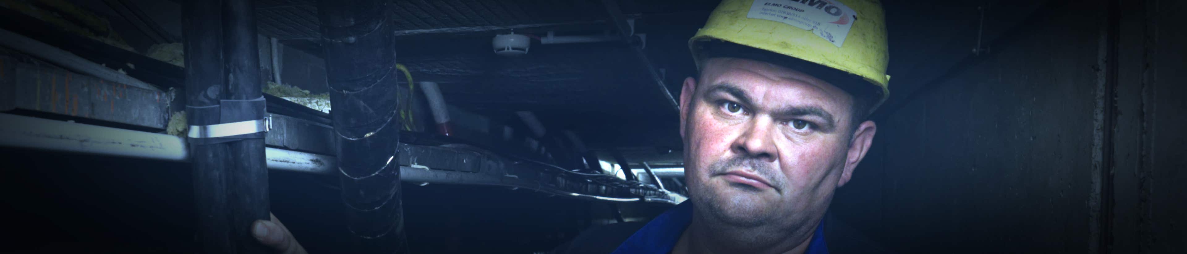 Team und Bauleiter Dieter Posniak in Kabeltunnel, mit Sicherheitshelm, Portraitausschnitt, schaut in Kamera