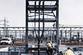 Baustelle Umspannwerk mit Industrieelektrikern und Kabelziehern - Baustelle Umspannwerk mit Industrieelektrikern und Kabelziehern an Kabelmast arbeitend, im Vordergrund, triste Winterathmosphaere, grauer Wolkenhimmel