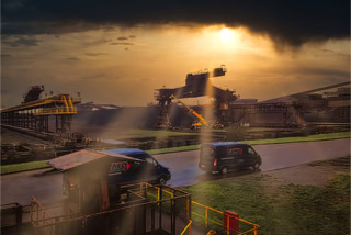 Eisenerz-Haldenanlage Stahlwerk Duisburg mit Teambussen Elmo Group im Vordergrund - Regennasse Eisenerz-Haldenanlage Stahlwerk Duisburg mit Teambussen Elmo Group im Vordergrund, aufbrechende, goldene Wolkendecke gibt tief stehende Sonne frei