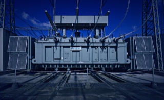 Leistungen - Transformatoren nach Anforderung - Wir liefern und installieren Öl- und Trockentransformatoren für jeden Bedarf - Öl-Transformator von Siemens, groß wie ein Haus, in Umspannwerk, blauer Himmel am Mittag