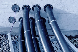 Sieben Oberschenkel dicke, schwarz ummantelte Niederspannungskabel auf metallender Kabeltrassen-Konstruktion verschwinden in Betonwand - Projekt Produktionsanlage Solarlux - Sieben Oberschenkel dicke, schwarz ummantelte Niederspannungskabel auf metallender Kabeltrassen-Konstruktion verschwinden in grauer Betonwand - Projekt Produktionsanlage Solarlux