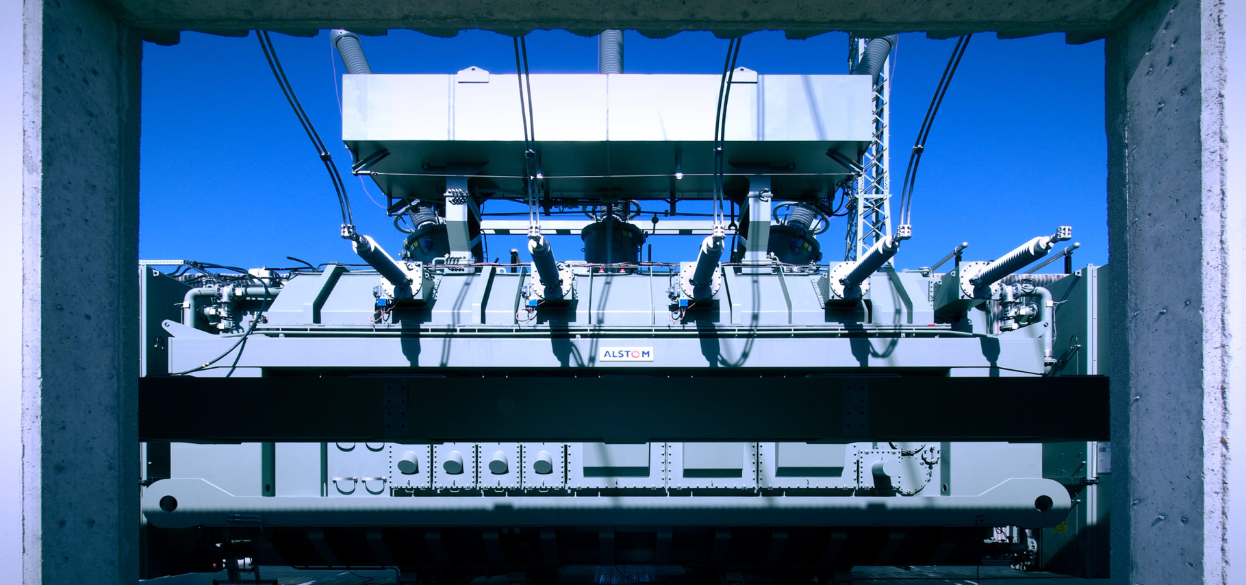 Foto gro&szlig;er Siemens Oel-Transformator in Umspannwerk, Blick durch Beton-Zarge, blauer Himmel