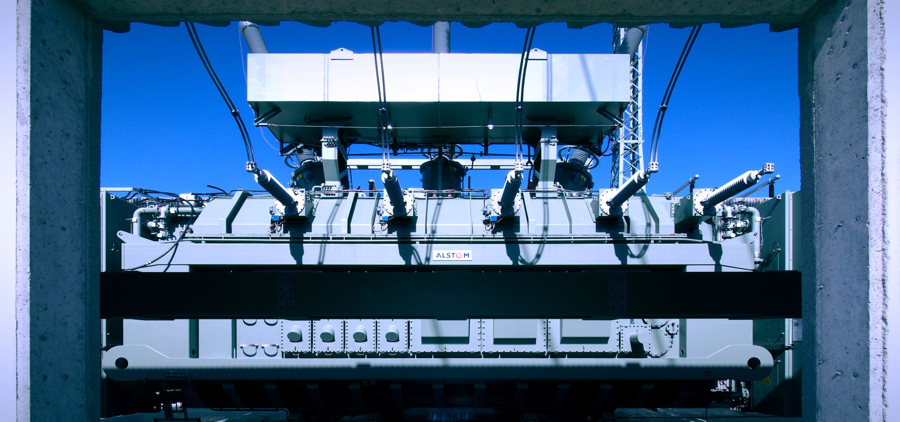 Foto großer Siemens Oel-Transformator in Umspannwerk, Blick durch Beton-Zarge, blauer Himmel