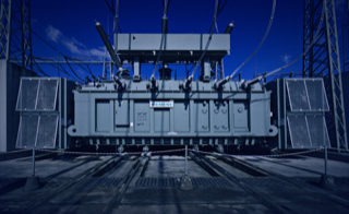 Leistungen - Transformatoren nach Anforderung - Wir liefern und installieren &Ouml;l- und Trockentransformatoren f&uuml;r jeden Bedarf - &Ouml;l-Transformator von Siemens, gro&szlig; wie ein Haus, in Umspannwerk, blauer Himmel am Mittag