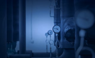 Leistungen - Mess- und Regeltechnik - Wir planen, konfigurieren und installieren industrielle Mess- und Regeltechnik - Senkrecht verlaufende Rohre, Industrieanlage mit runden Messanzeigen, Unschärfe nach Hinten