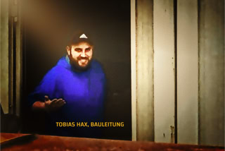Bauleiter Tobias Hax - Bauleiter Tobias Hax mit blauem Hoody und Baseball-Cap laechelt in Kamera
