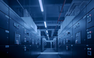 Leistungen - &Uuml;berwachungstechnik - Wir konzipieren und installieren Technik zur Prozesssteuerung - Blick in langen Gang mit Schaltschrankanlagen links und rechts, leuchtende gr&uuml;ne und rote L&auml;mpchen