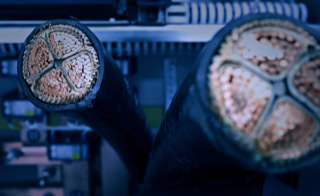 Engineering - Ingenierleistungen Elmo Group - Unser Portfolio umfasst Ingenieurleistungen wie z.B. die Berechnung von Biegeradien, die kurzschlu&szlig;feste B&uuml;ndelung von Kabelmontagen oder die Berechnung der Lastenverteilung von Kabelb&uuml;hnen - Vieladrige Niederspannungskabelenden/Querschnitt im Bildvordergrund, unscharfer Schaltschrank im Hintergrund